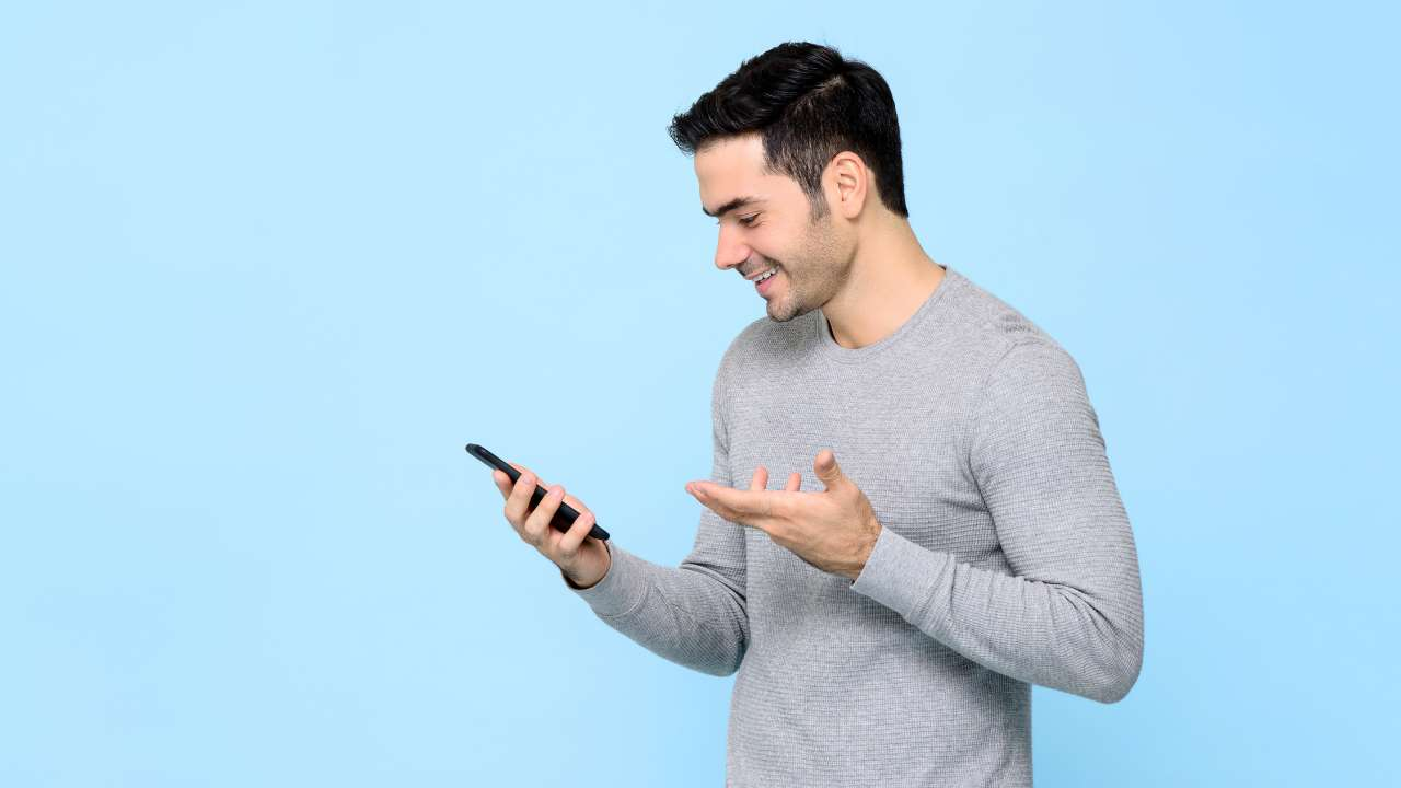 Smaidīgs vīrietis ar prieku skatās savā viedtālrunī, jo ir saņēmis apstiprinājumu aizdevumam līdz algai